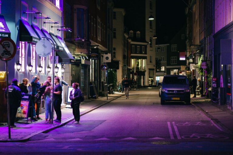 Explore Copenhagen's vibrant nightlife with people enjoying the city streets under purple lights.