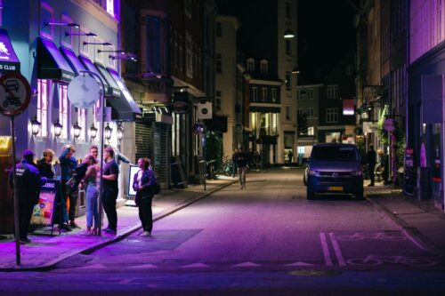 Explore Copenhagen's vibrant nightlife with people enjoying the city streets under purple lights.
