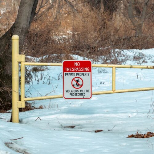A 'No Trespassing' sign on a yellow gate in a snowy forest, indicating private property during winter.