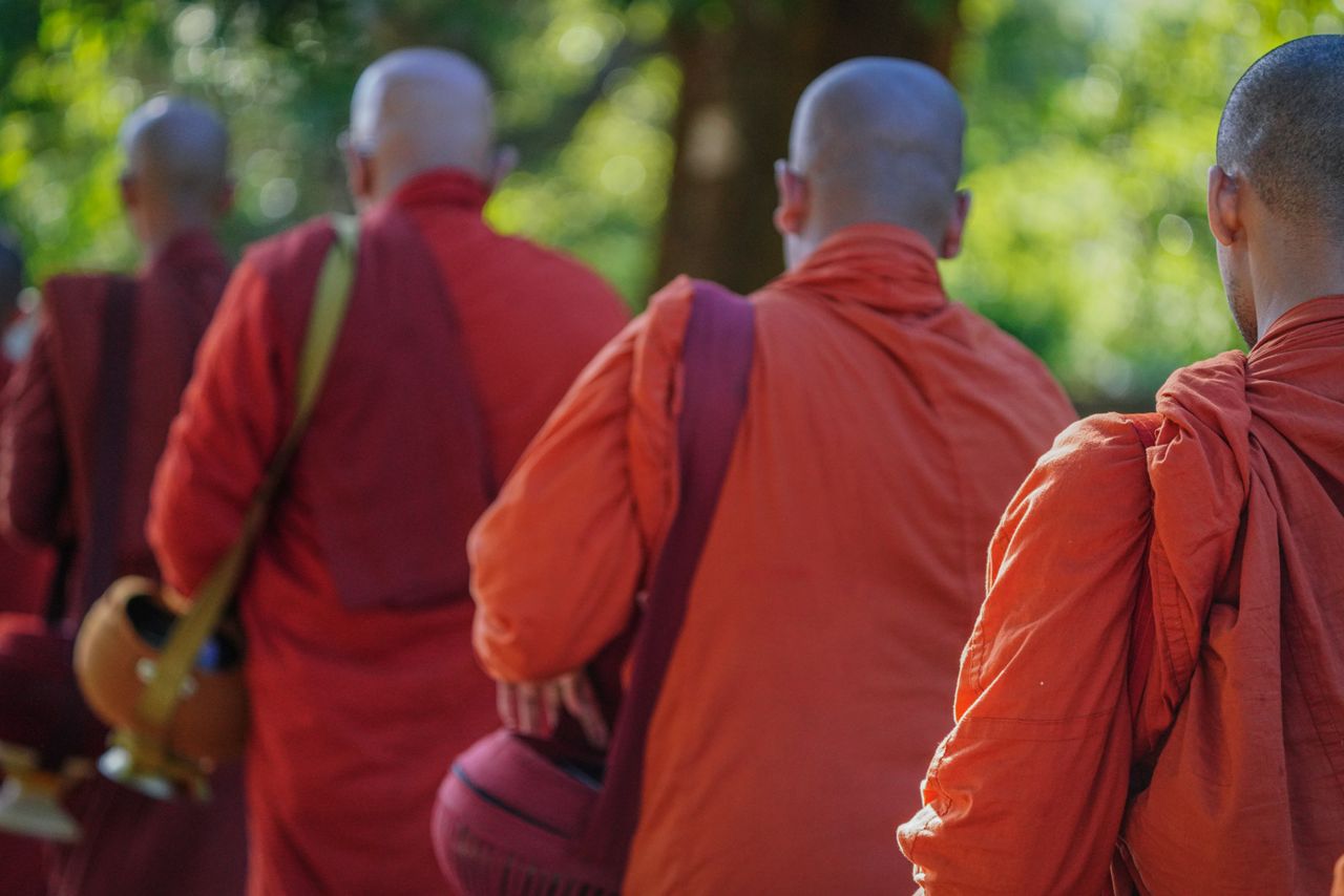 A group of Buddhist monks in traditional orange robes participating in a pilgrimage on a sunny day in Sri Lanka.