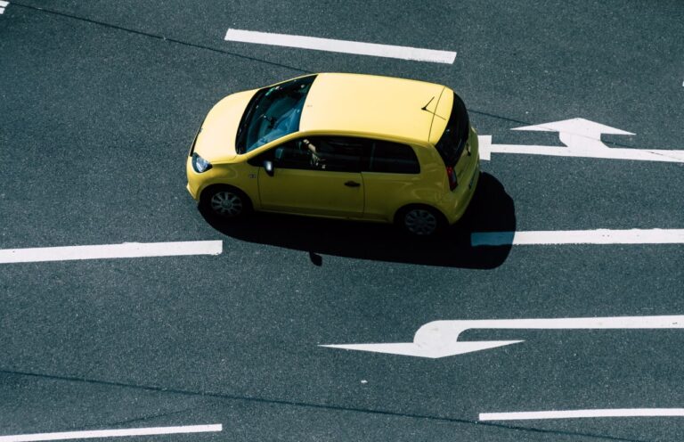 Aerial view of a yellow car on a road with directional arrows, highlighting urban transport.
