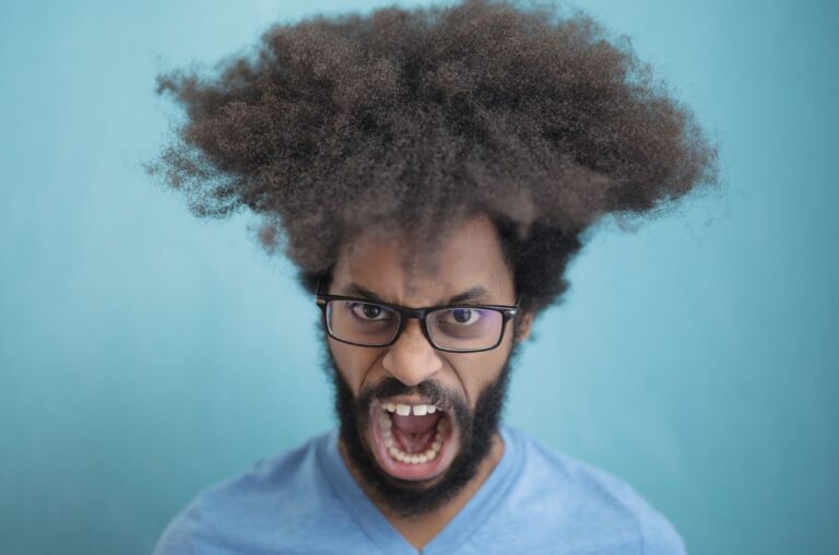 Portrait of a man with afro hair wearing eyeglasses, expressing emotion against a blue background.