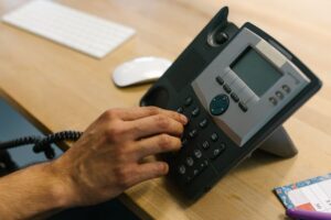 บทความที่ 17 : ทวงหนี้อย่างไร ไม่ผิดกฎหมาย A hand dialing a phone on a wooden desk. Office environment with keyboard and planner.