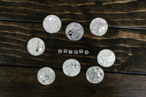 Silver cryptocurrency coins arranged on a wooden surface spelling 'crypto'.